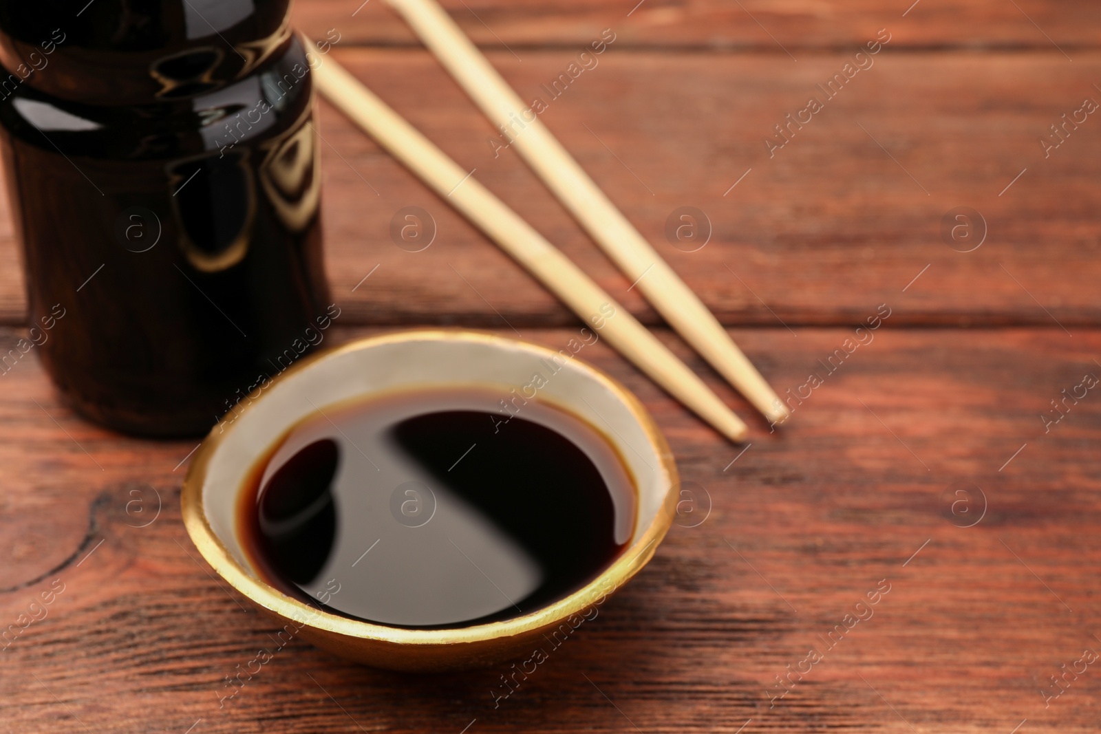 Photo of Bottle, bowl with soy sauce and chopsticks on wooden table, closeup. Space for text