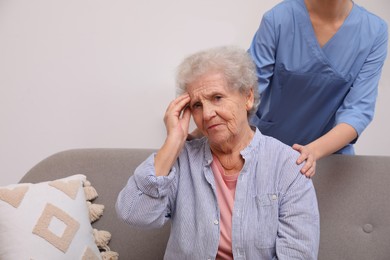 Photo of Nurse taking care of senior woman with headache indoors