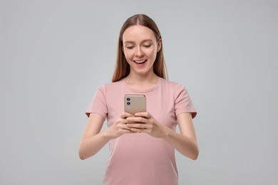 Woman sending message via smartphone on grey background, space for text