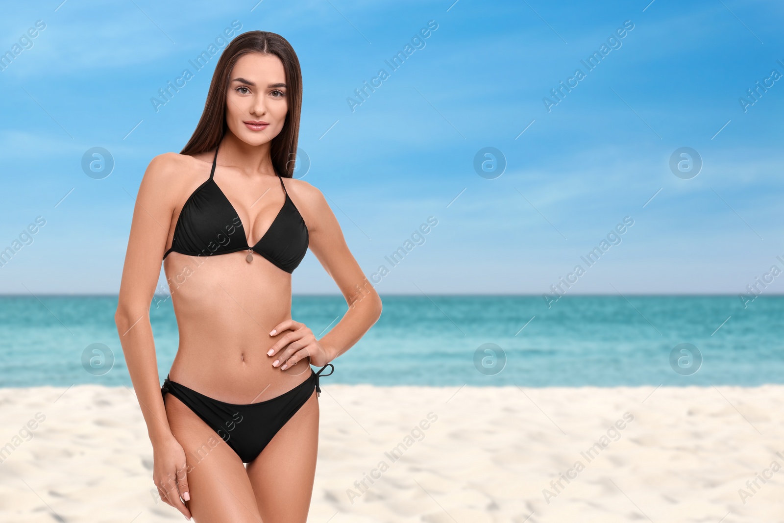 Image of Beautiful woman in stylish black bikini on sandy beach near sea, space for text