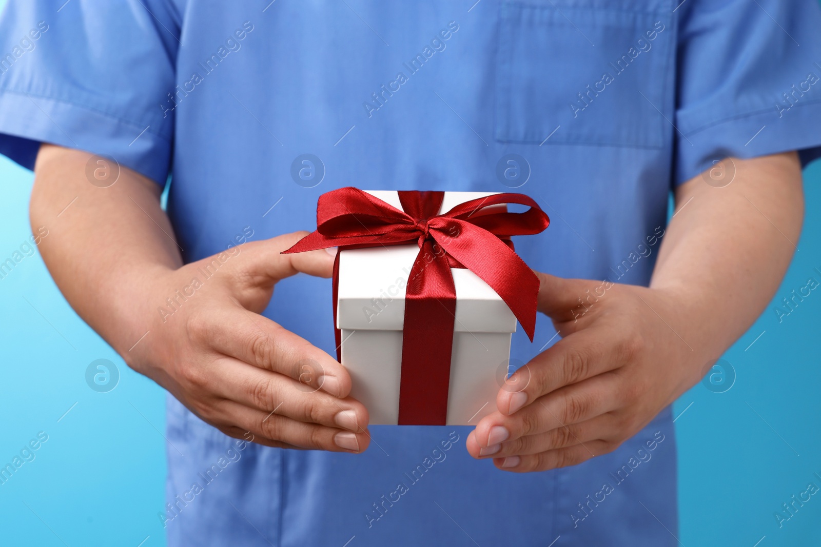 Photo of Doctor holding gift box on light blue background, closeup. Medical present