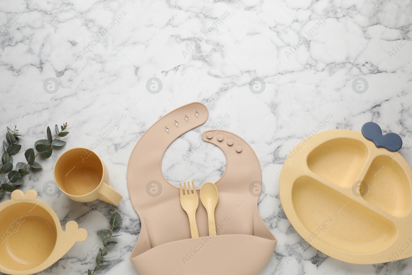 Photo of Flat lay composition with silicone baby bib and plastic dishware on white marble background. Space for text