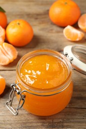 Photo of Tasty tangerine jam in glass jar on wooden table