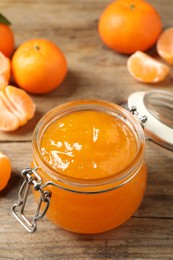 Tasty tangerine jam in glass jar on wooden table