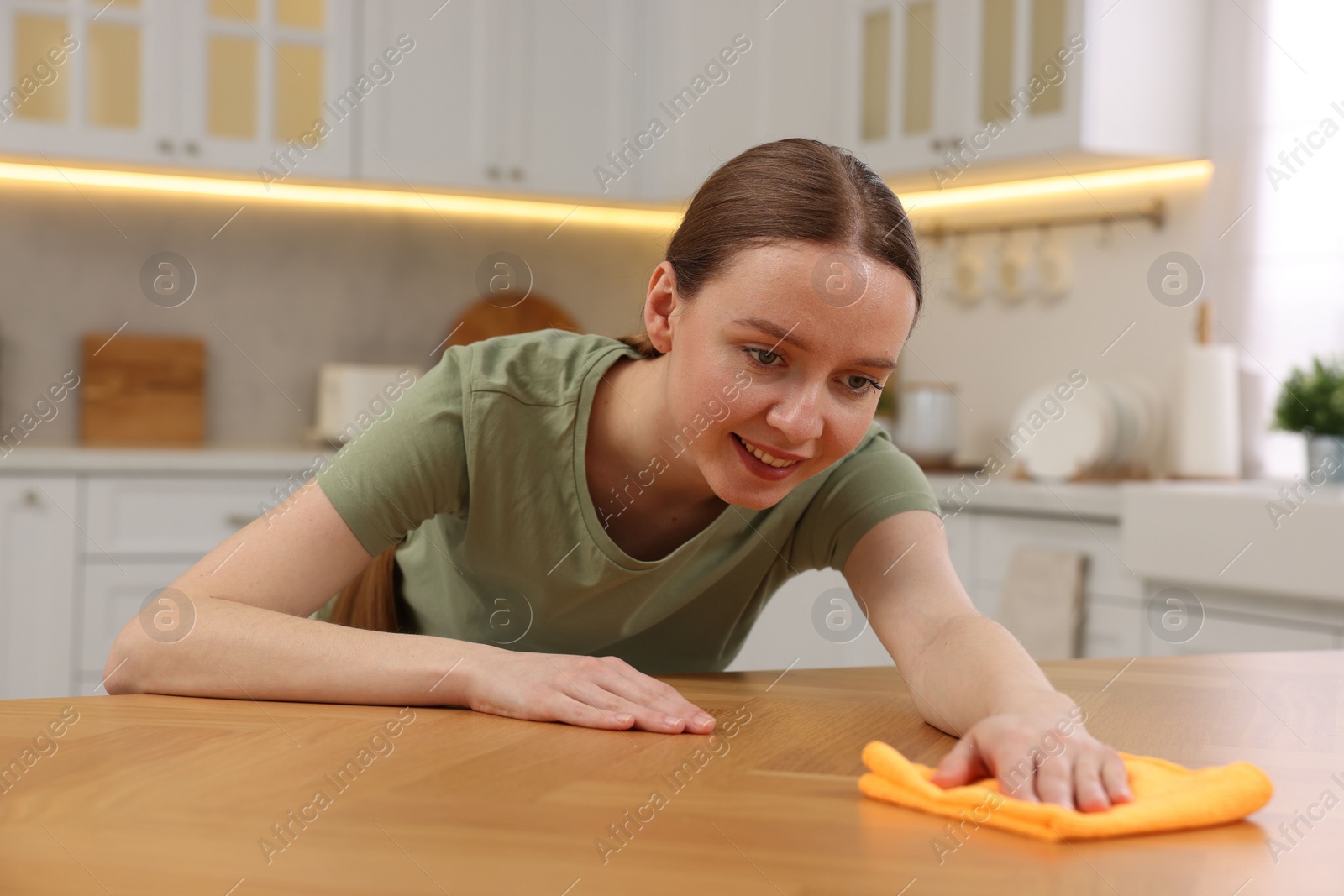 Photo of Woman with microfiber cloth cleaning wooden table in kitchen