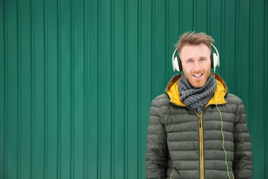 Young man listening to music with headphones against color wall. Space for text