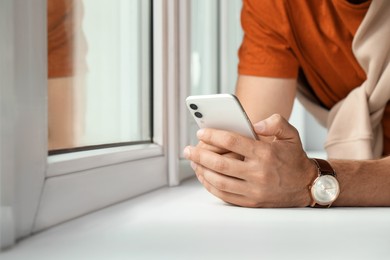 Photo of Man using smartphone near window, closeup. Space for text