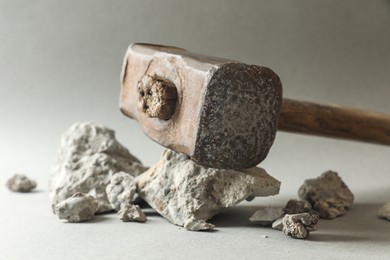 Photo of One sledgehammer and pieces of broken stones on grey background, closeup