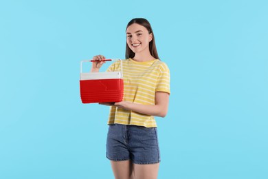 Happy young woman with plastic cool box on light blue background