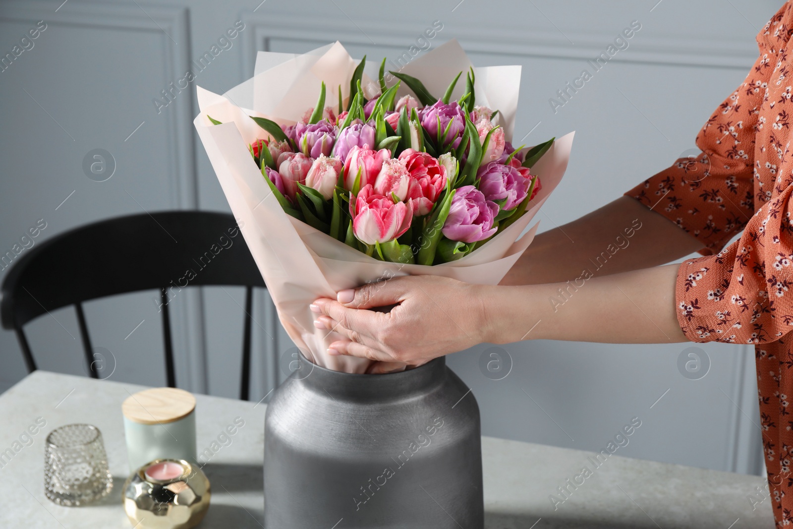 Photo of Woman putting bouquet of beautiful tulips in vase indoors, closeup