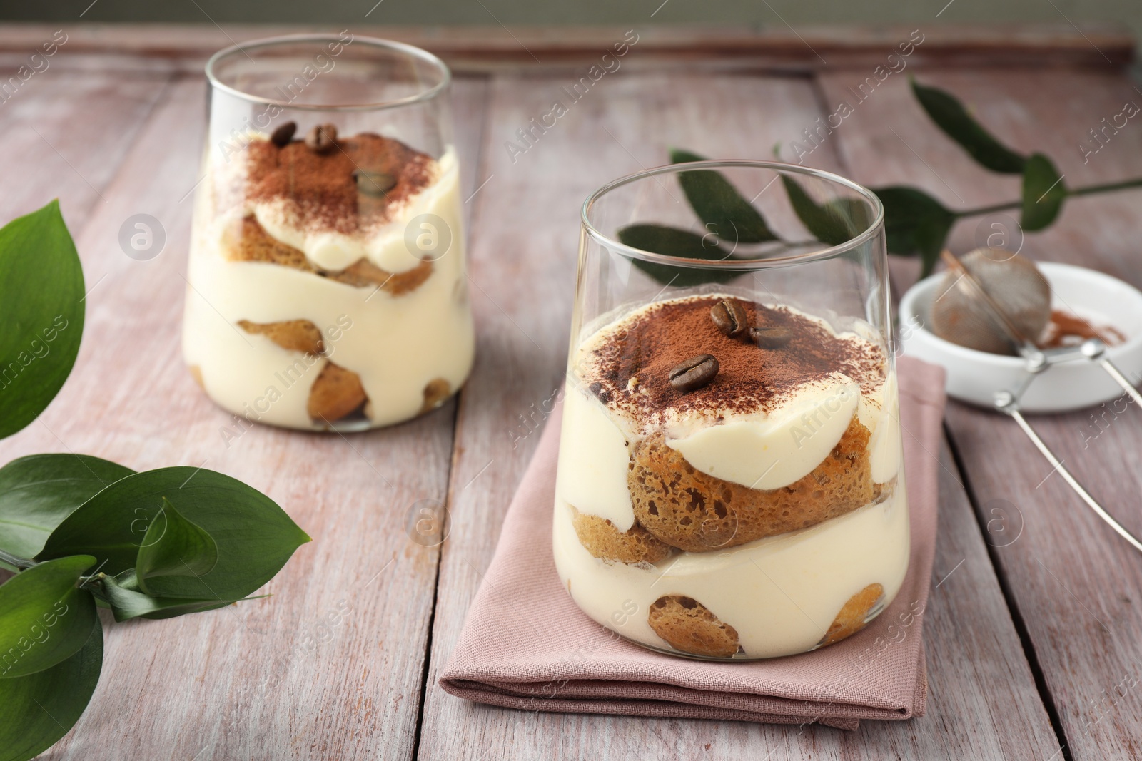 Photo of Delicious tiramisu with coffee beans in glasses and green leaves on wooden table