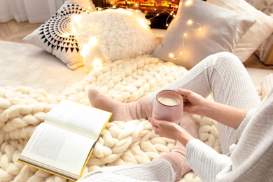 Photo of Woman with cup of coffee and book sitting on soft plaid, closeup