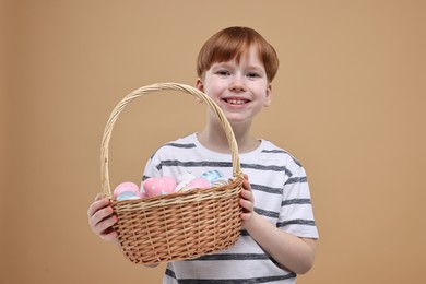 Photo of Easter celebration. Cute little boy with wicker basket full of painted eggs on dark beige background