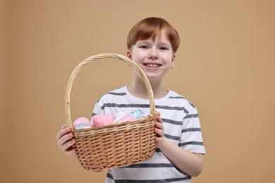 Easter celebration. Cute little boy with wicker basket full of painted eggs on dark beige background