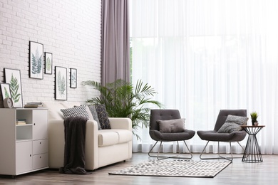 Photo of Comfortable sofa and chairs near window with elegant curtains in room