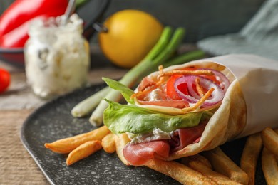 Photo of Delicious pita wrap with prosciutto, vegetables and potato fries on wooden table, closeup