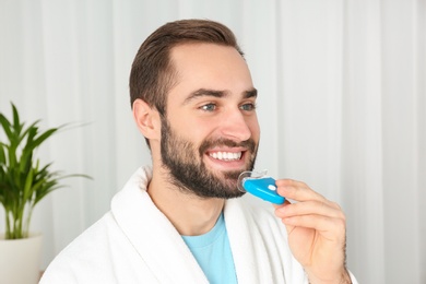 Photo of Young man using teeth whitening device at home