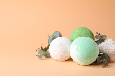 Photo of Colorful bath bombs, salt and eucalyptus branches on beige background, space for text