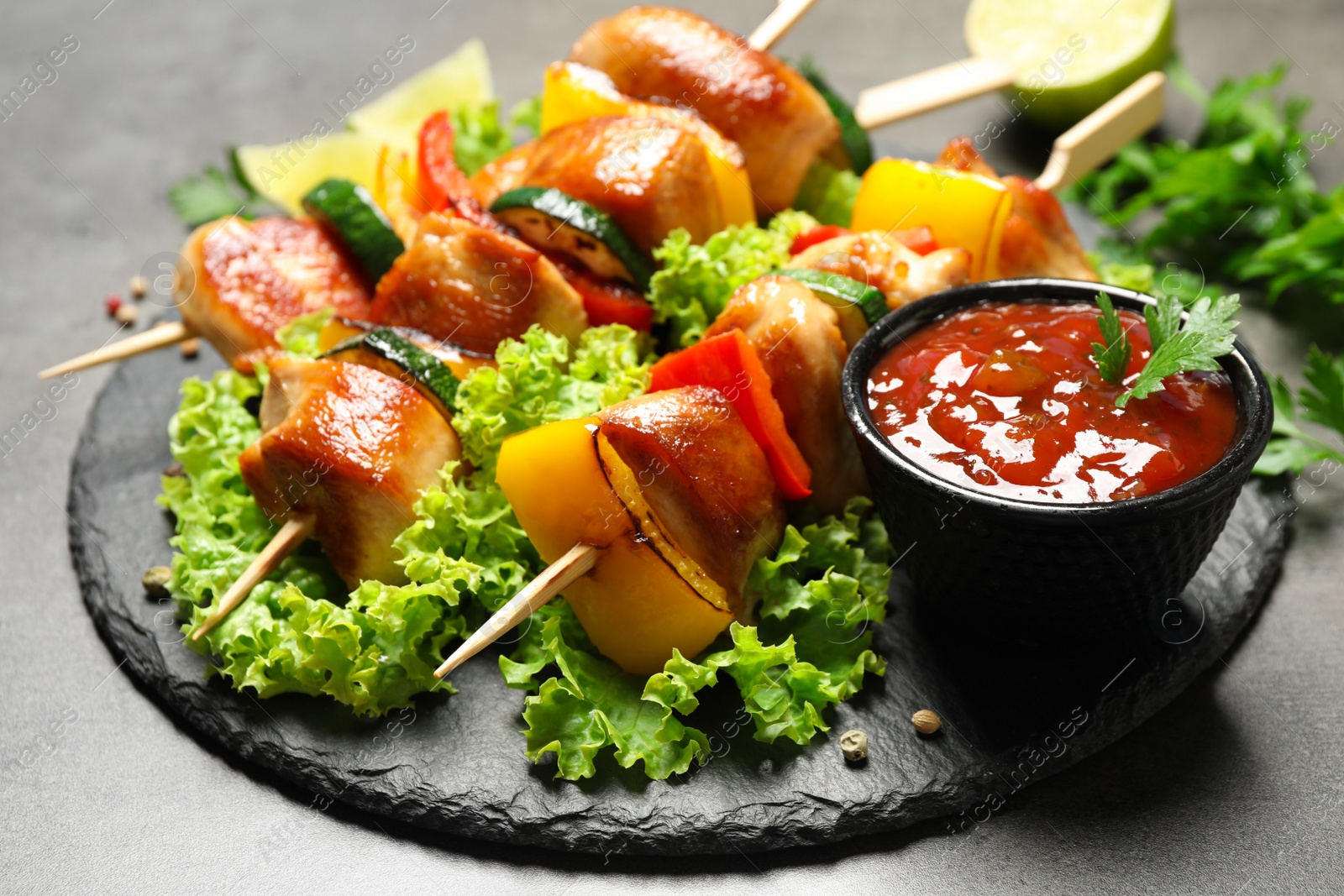 Photo of Delicious chicken shish kebabs with vegetables and ketchup on grey table, closeup