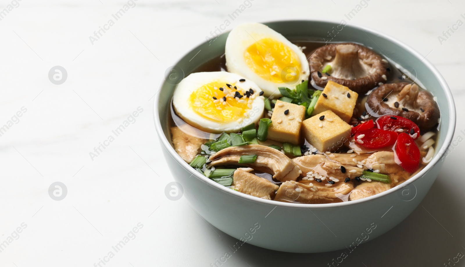 Photo of Bowl of delicious ramen on white table, space for text. Noodle soup