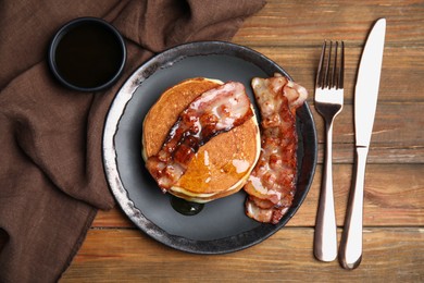 Delicious pancakes with maple syrup and fried bacon on wooden table, flat lay