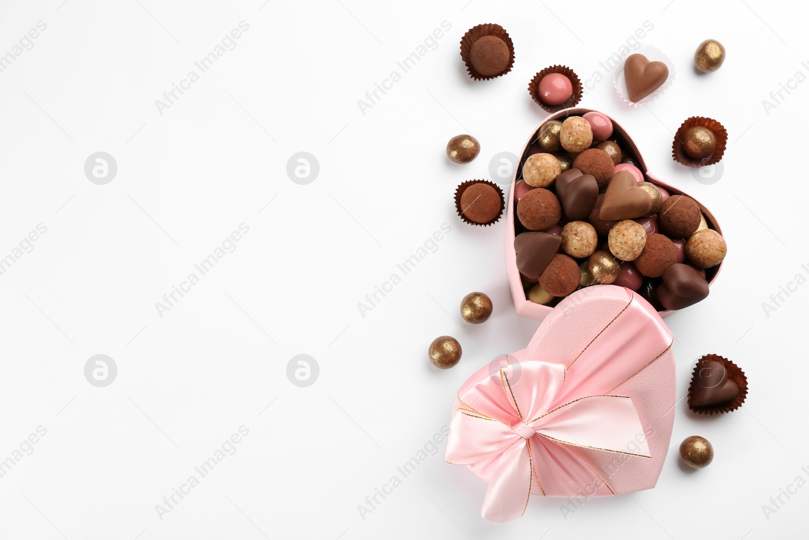 Photo of Different delicious chocolate candies in heart shaped box on white background, flat lay. Space for text