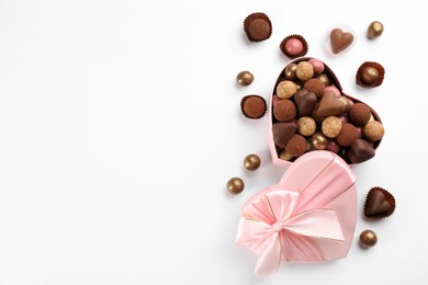 Photo of Different delicious chocolate candies in heart shaped box on white background, flat lay. Space for text