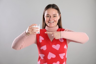 Photo of Happy woman with milk mustache pointing at glass of drink on light grey background