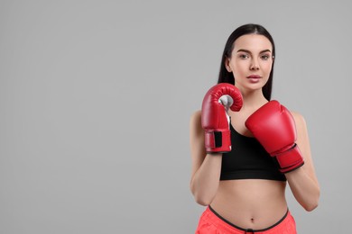 Portrait of beautiful woman in boxing gloves on grey background. Space for text