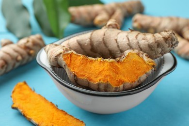 Bowl with turmeric roots on light blue table, closeup