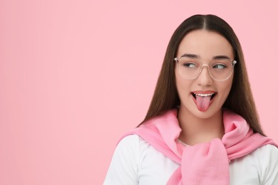 Happy woman showing her tongue on pink background, space for text