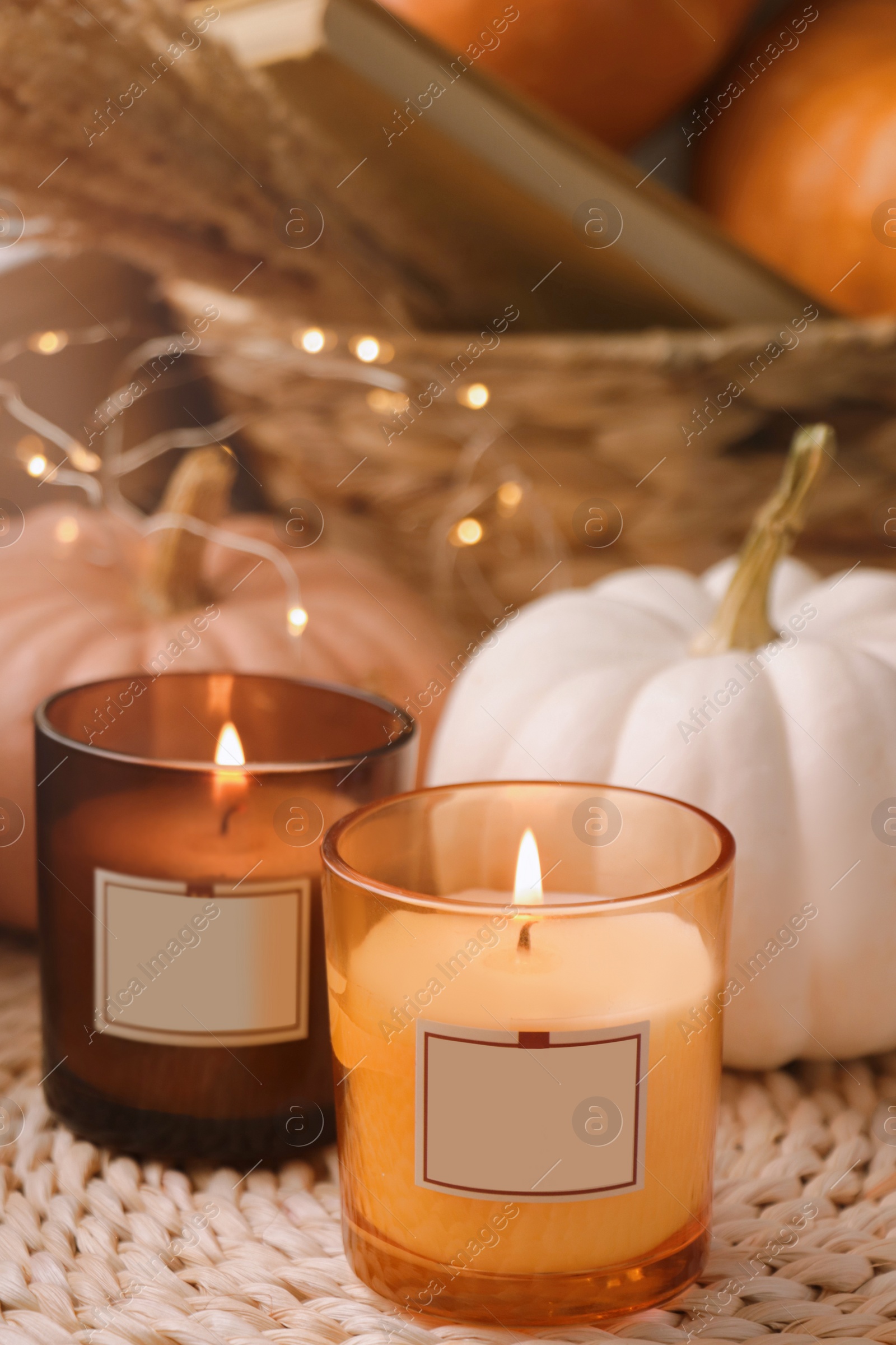 Photo of Scented candles and pumpkins on wicker mat indoors