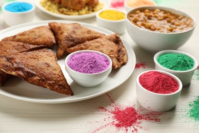 Traditional Indian food and color powders on white wooden table, closeup. Holi festival celebration