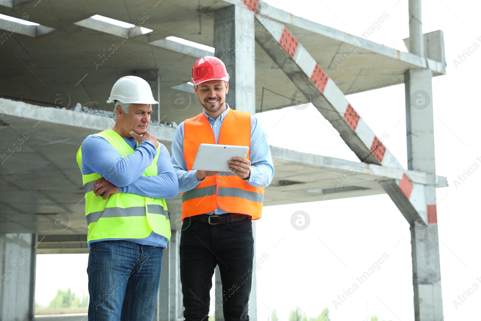 Photo of Professional engineer with tablet and foreman in safety equipment at construction site. Space for text