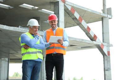Photo of Professional engineer with tablet and foreman in safety equipment at construction site. Space for text