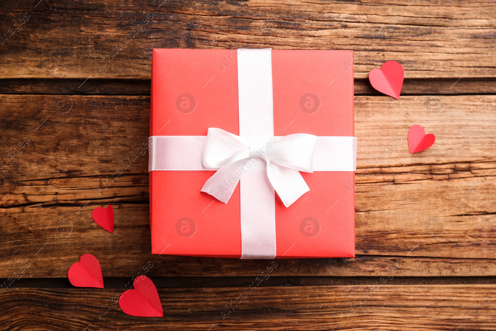 Photo of Beautiful gift box and paper hearts on wooden table, flat lay. Valentine's Day celebration