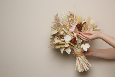 Photo of Woman holding beautiful dried flower bouquet on beige background, closeup. Space for text