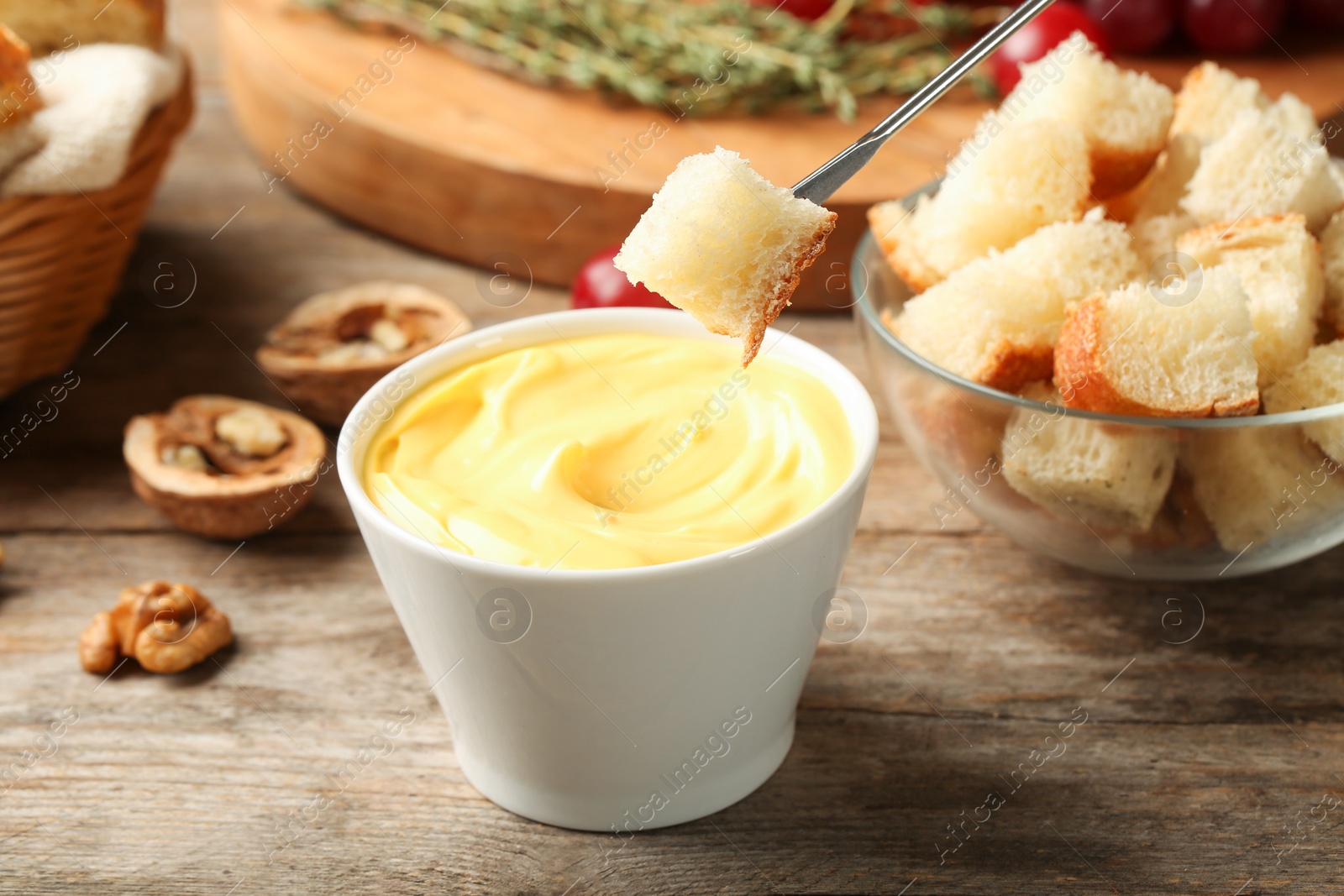 Photo of Piece of bread over bowl with delicious cheese fondue on wooden table