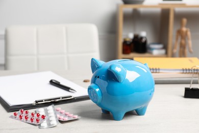 Photo of Blue piggy bank near pills and clipboard on wooden table in hospital. Medical insurance