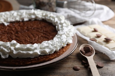 Photo of Delicious homemade sponge cake with cream and different kinds of chocolate on wooden table, closeup