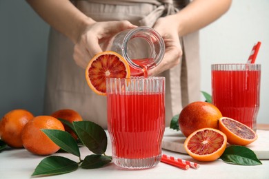 Photo of Woman pouring tasty sicilian orange juice into glass at white wooden table, closeup