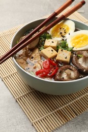 Photo of Bowl of delicious ramen and chopsticks on grey table, closeup. Noodle soup