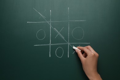 Photo of Woman playing tic tac toe game on green chalkboard, top view