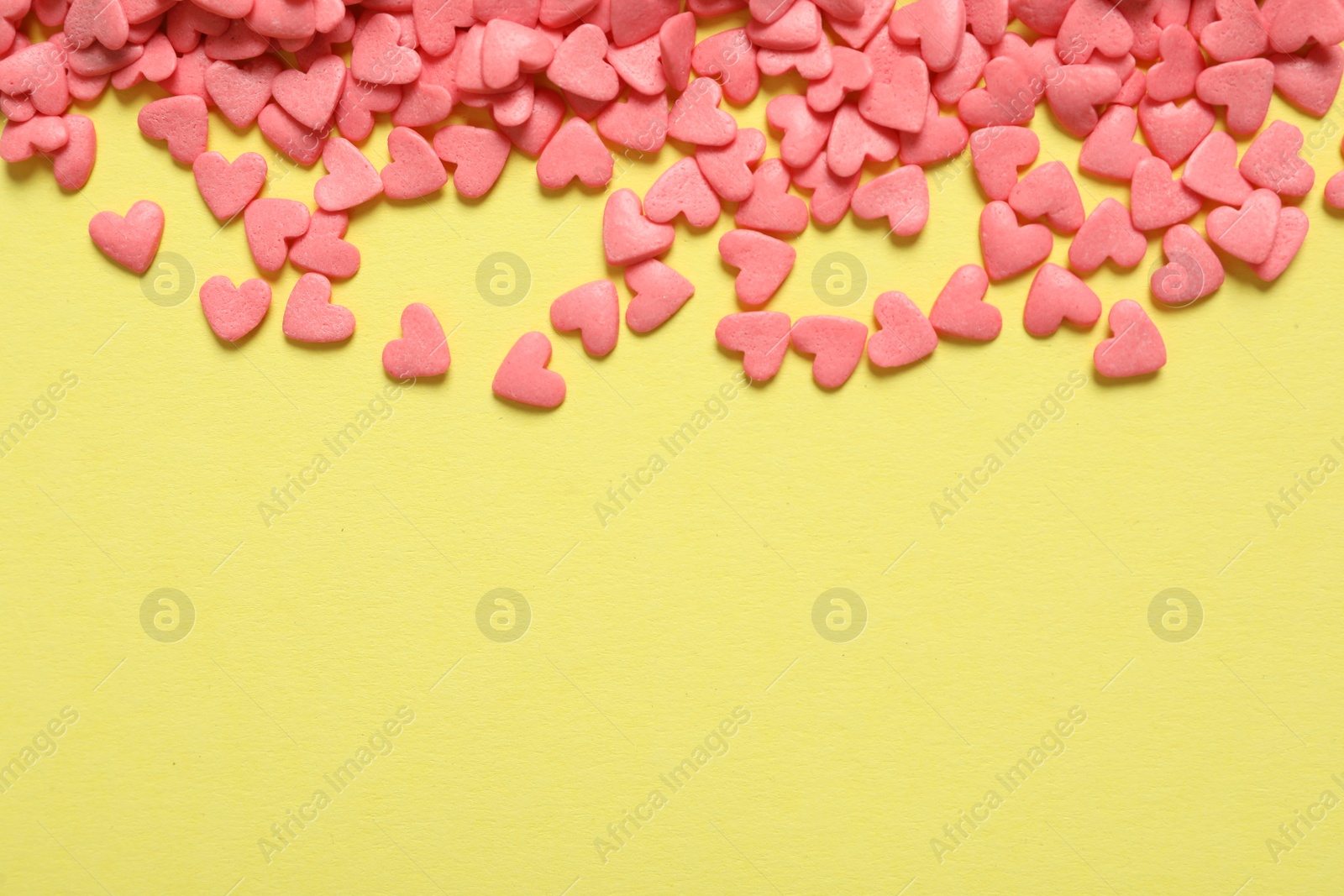 Photo of Bright heart shaped sprinkles on yellow background, flat lay. Space for text