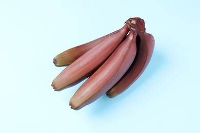 Tasty red baby bananas on light blue background, top view