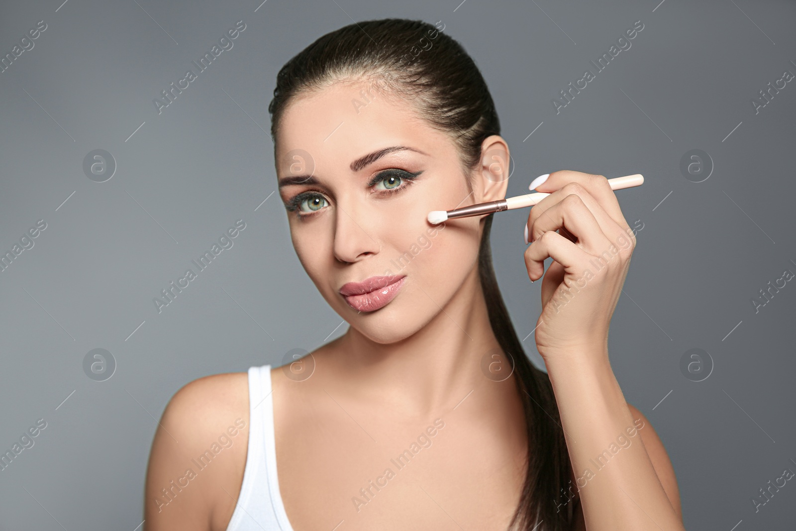 Photo of Beautiful woman applying makeup with brush on light grey background