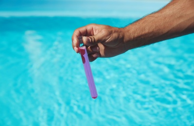 Photo of Man holding test tube with reagent near swimming pool, closeup