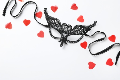 Photo of Black lace mask for sexual role play and red hearts on white background