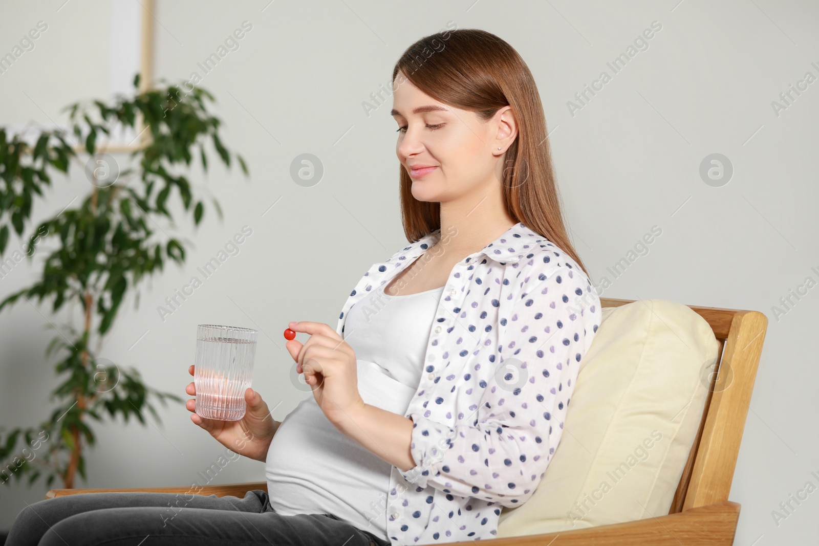 Photo of Beautiful pregnant woman holding pill and glass of water at home