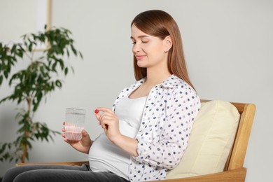 Beautiful pregnant woman holding pill and glass of water at home